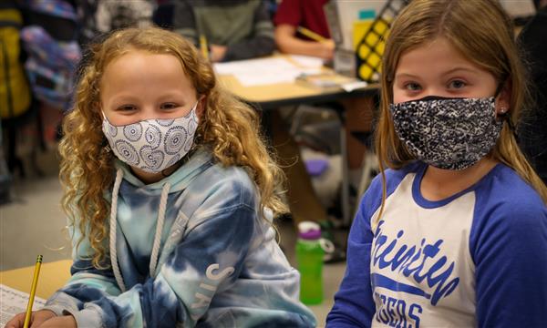 Two girls smile while wearing masks